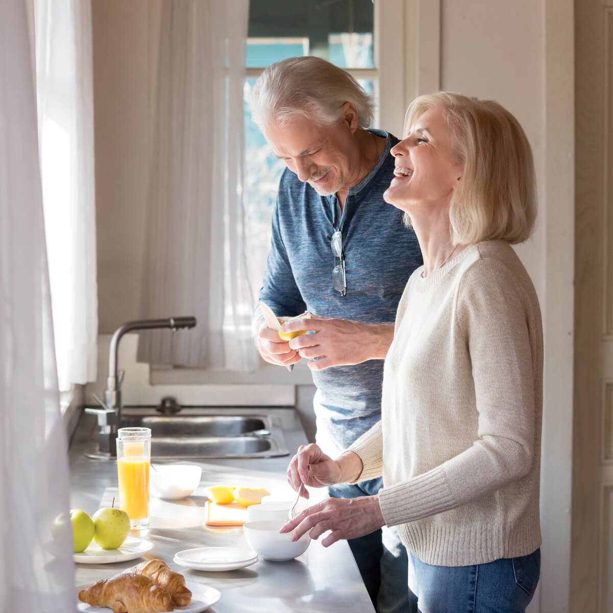 an elderly couple smiling whilst preparing breakfast in a light and airy kitchen